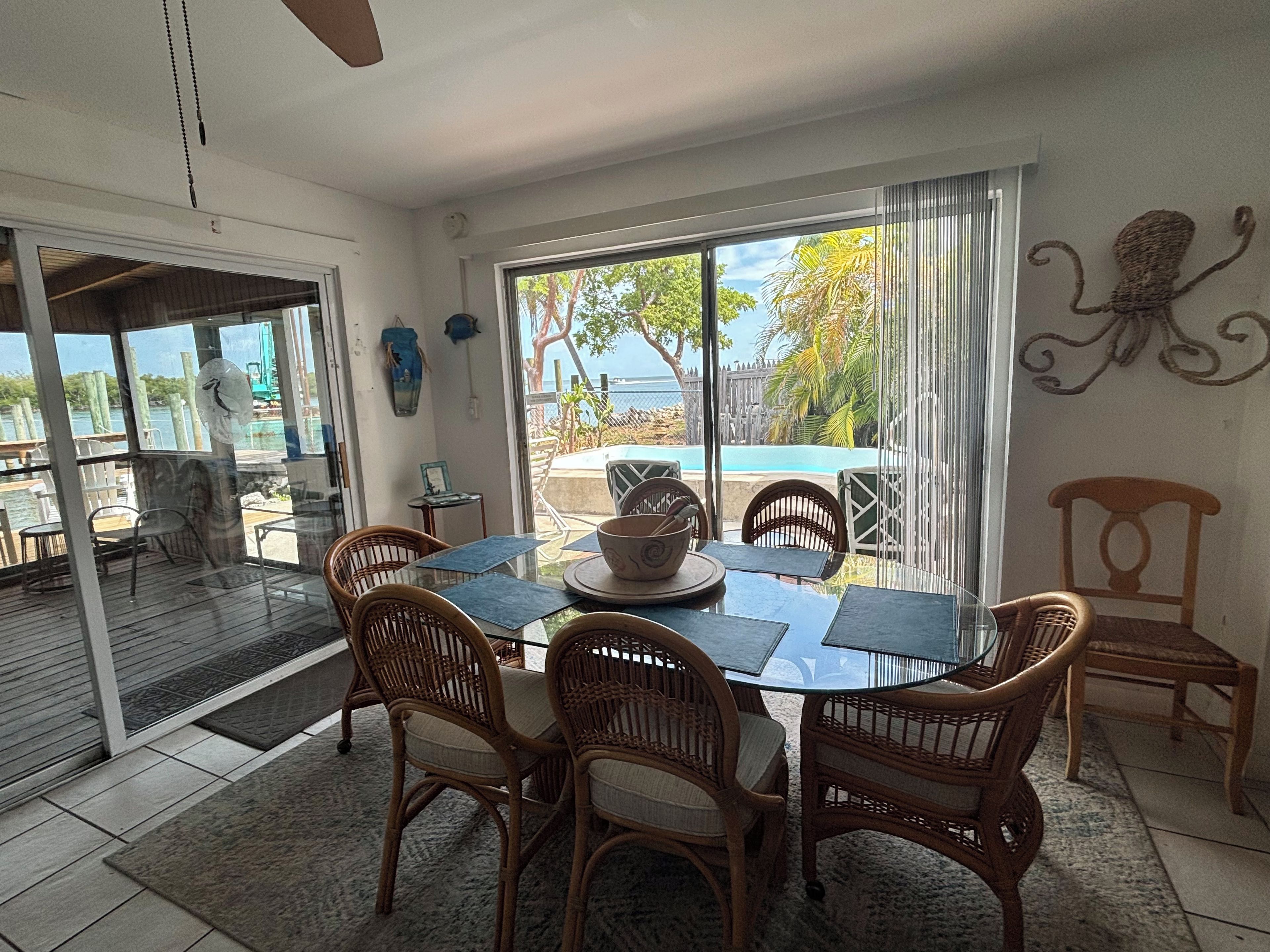 A dining area with a glass table and wicker chairs, overlooking a pool and greenery.