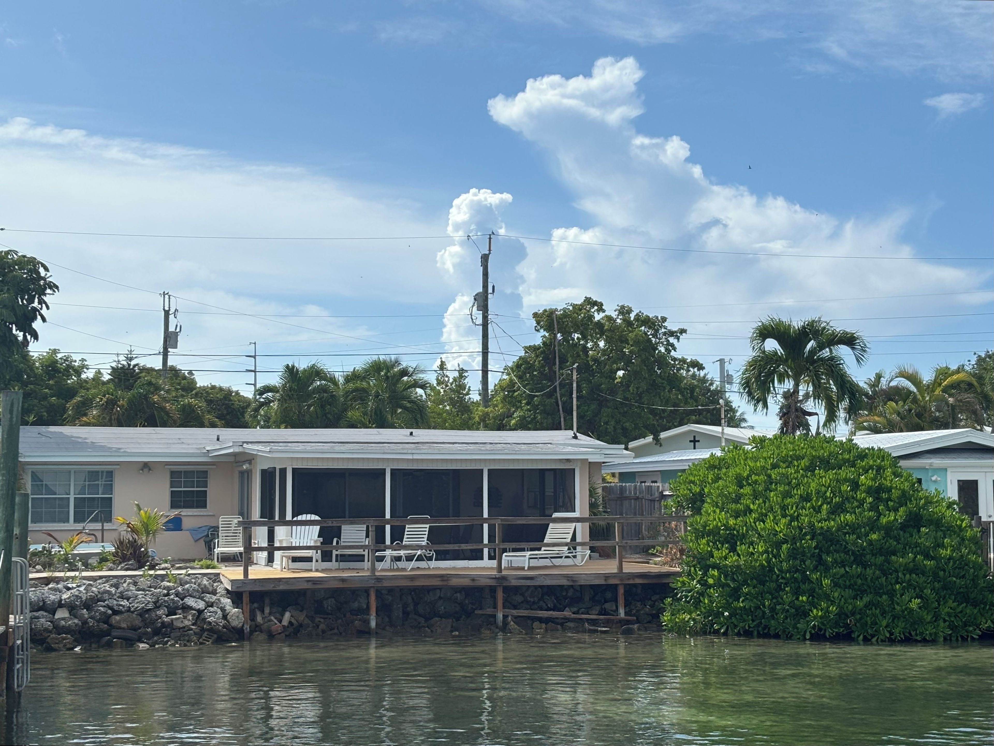 A waterfront property with a covered deck, lounge chairs, and a view of the water.