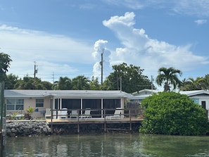 A waterfront property with a covered deck, lounge chairs, and a view of the water.