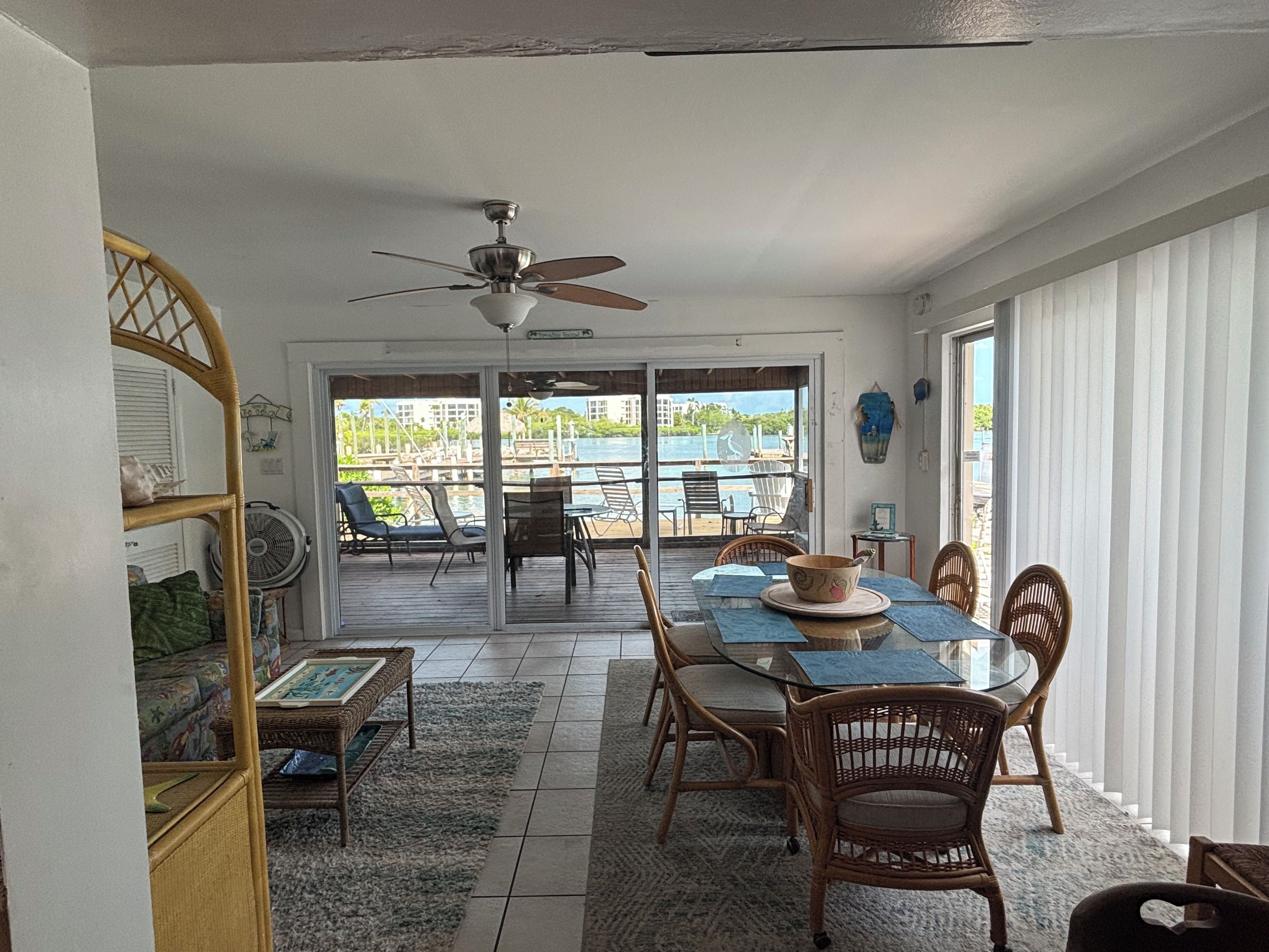 A dining area with a glass table, wicker chairs, and a view of a dock and water.