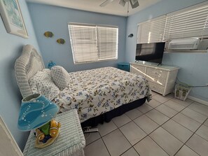 A bedroom with a bed, a television, a window with blinds, and a ceiling fan.