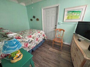 Een slaapkamer met een bed, een stoel, een televisie en een kleine tafel met een speeltje.