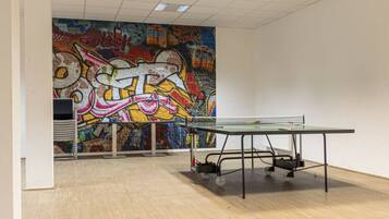 An indoor space with a ping pong table, a graffiti mural on the wall, and a whiteboard.
