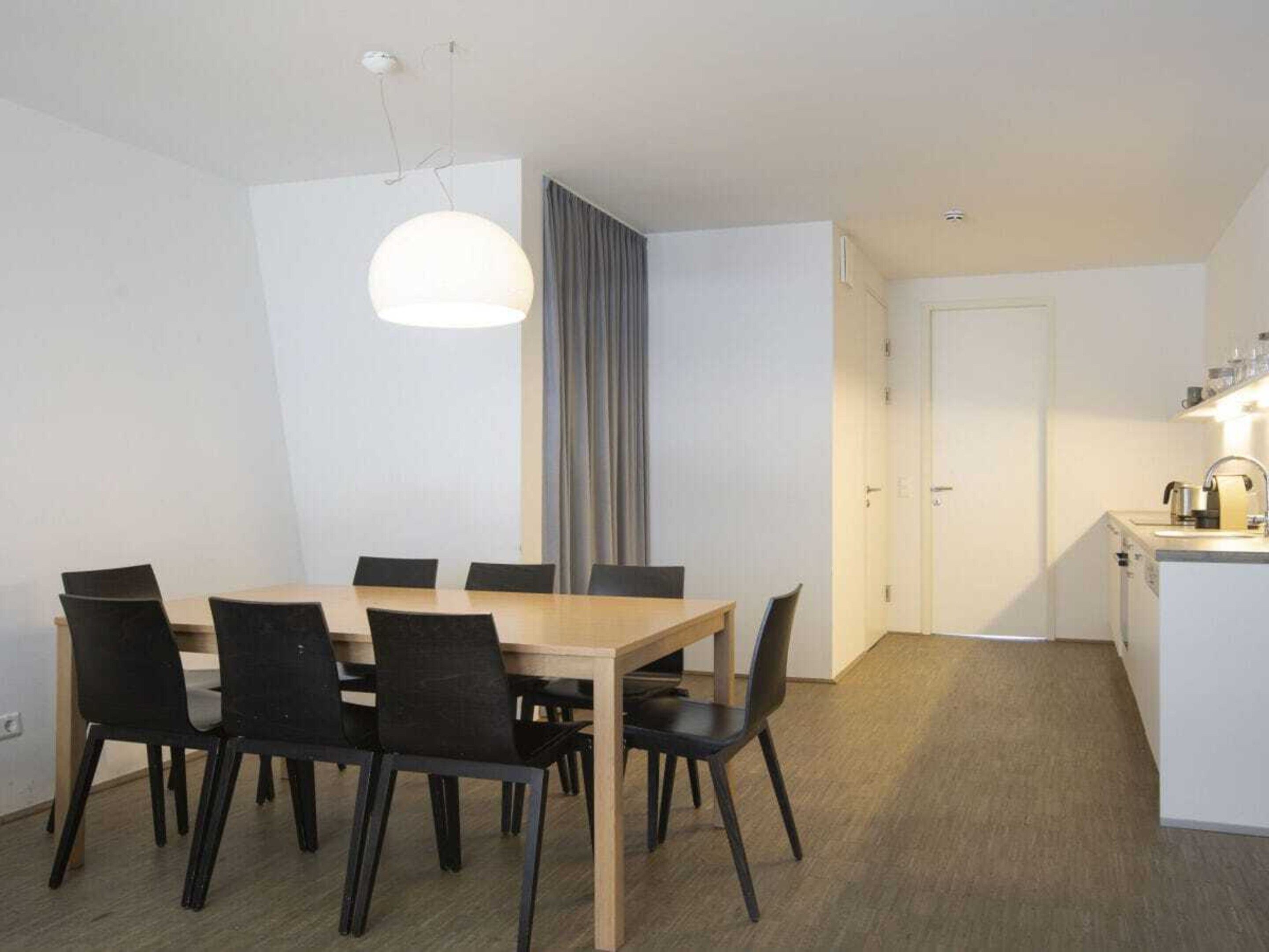 A modern dining area with a wooden table and black chairs, a pendant light, and a kitchen area with a sink and countertop.
