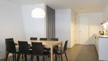 A modern dining area with a wooden table and black chairs, a pendant light, and a kitchen area with a sink and countertop.