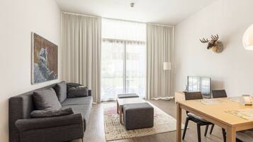 A modern living room with a grey sofa, a wooden dining table, and a large window with curtains.