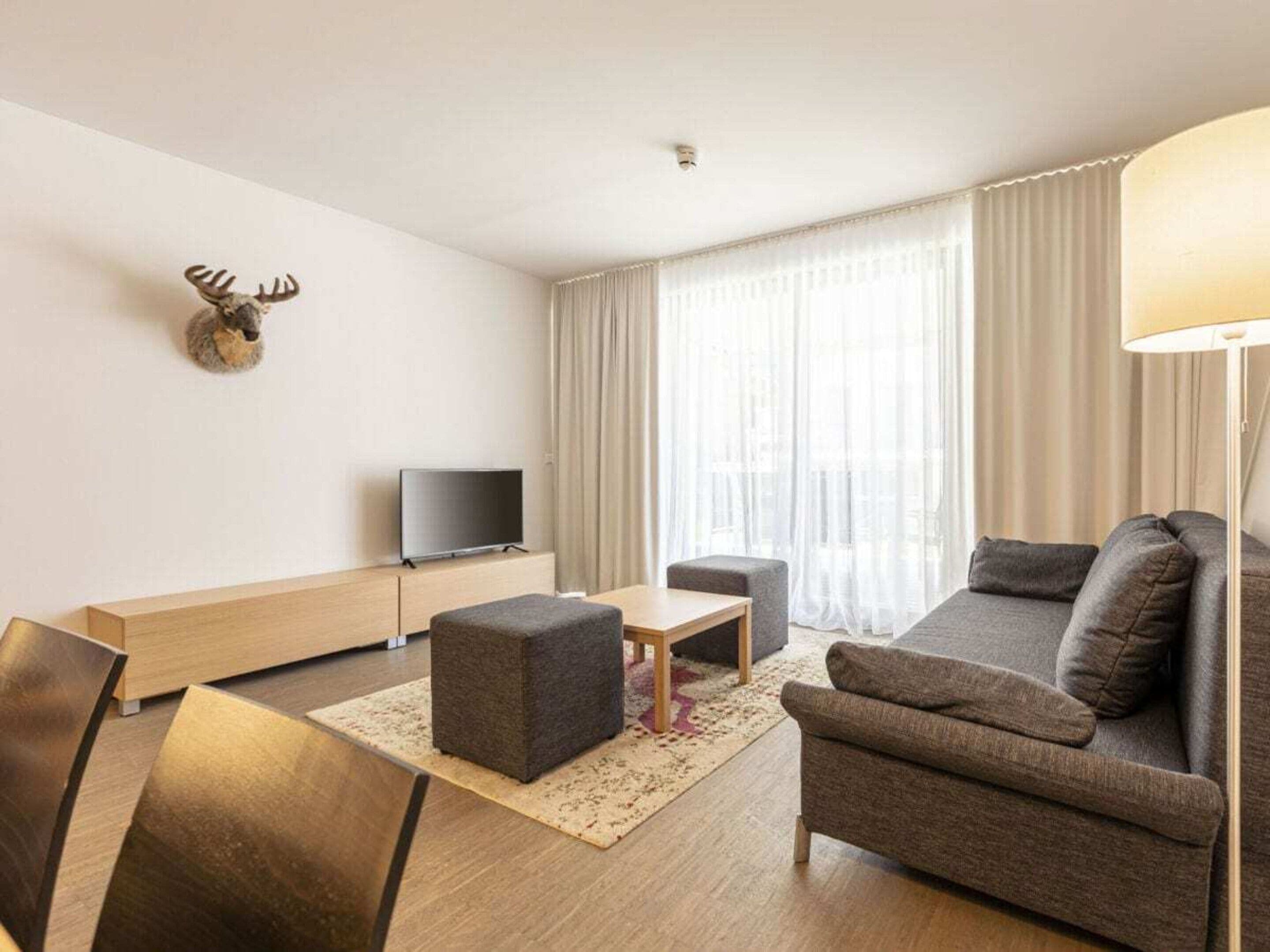 Een moderne woonkamer met een bank, een poef, een salontafel en een flatscreen televisie.