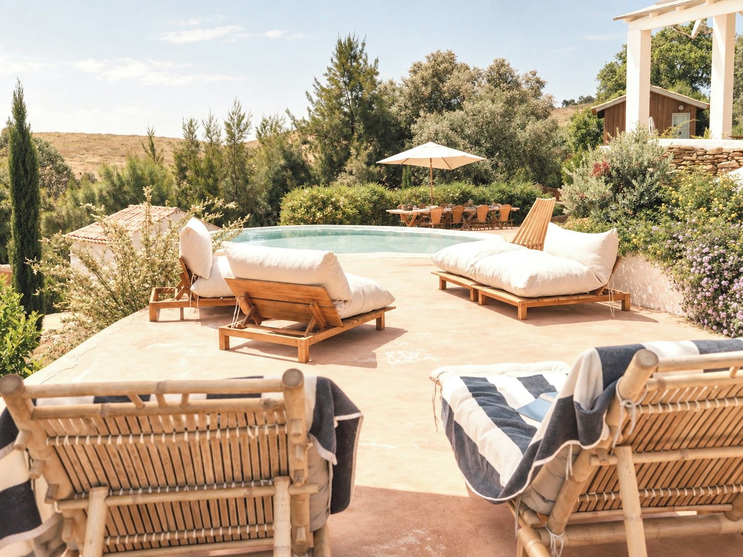 A poolside area with lounge chairs and a table, surrounded by greenery and a view of the landscape.