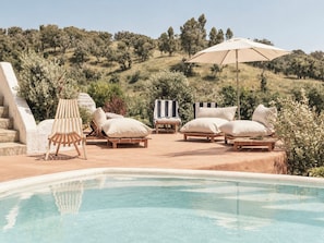 A poolside area with lounge chairs and a large umbrella. - Monte da Serra de Baixo (Sines)