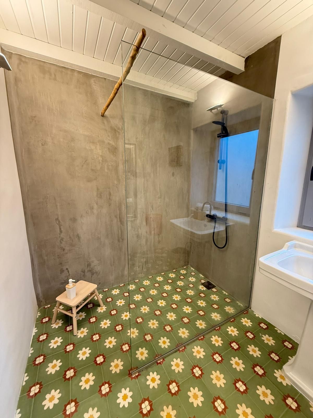 Een badkamer met een douche, een klein houten krukje en een betegelde vloer met een bloemenmotief.