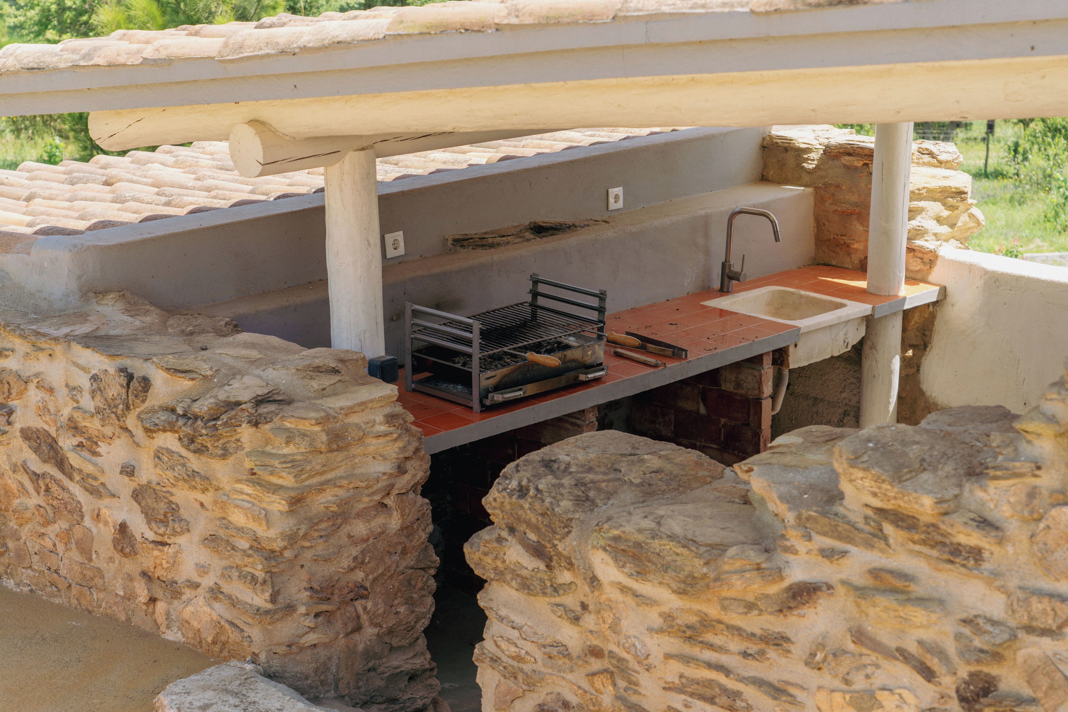 Un espace cuisine extérieur avec des murs en pierre, un barbecue en métal, un évier et un robinet.