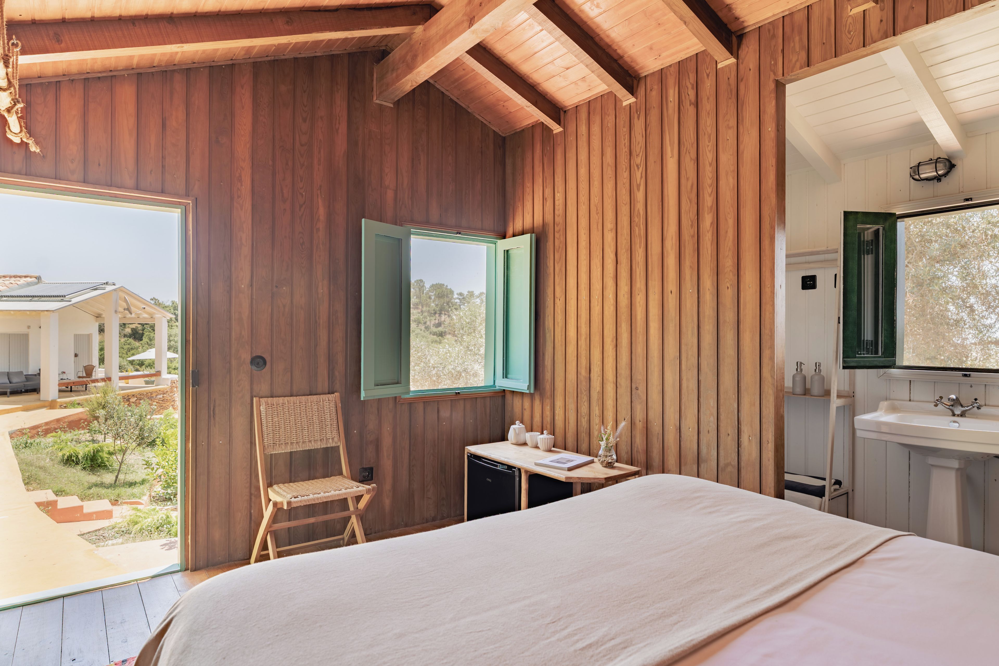 Une chambre à coucher avec un lit, une chaise, une petite table avec quelques objets, et une salle de bain avec un lavabo.
