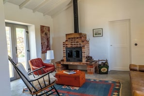 A living room with a brick fireplace, a red leather chair, a wooden chest, and a patterned rug. - Monte da Serra de Baixo (Sines)