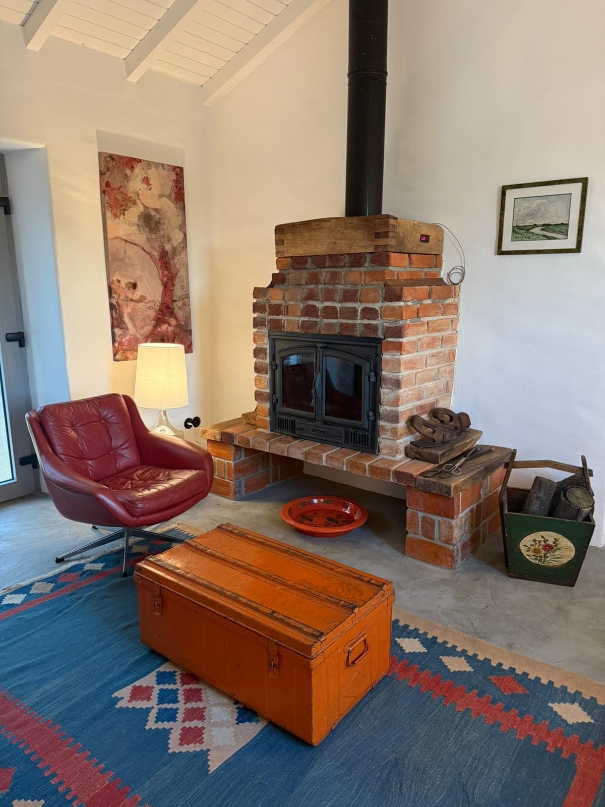 A room with a brick fireplace, a leather armchair, a wooden chest, and a colorful rug.