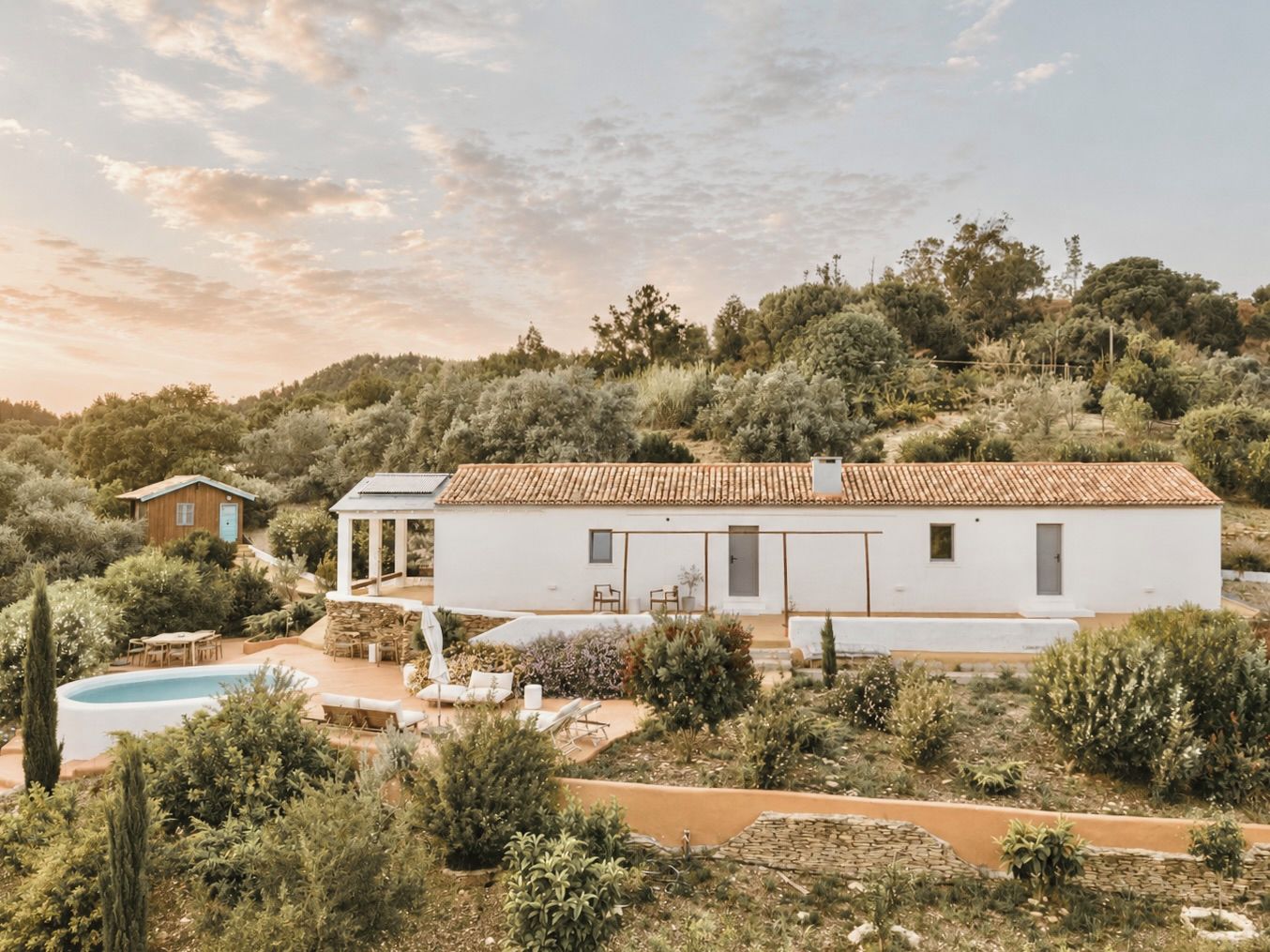 A white villa with a tiled roof, surrounded by lush vegetation and a pool.