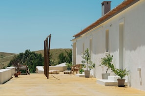 A patio area with a white building, potted plants, outdoor furniture, and a clear sky. - Monte da Serra de Baixo (Sines)