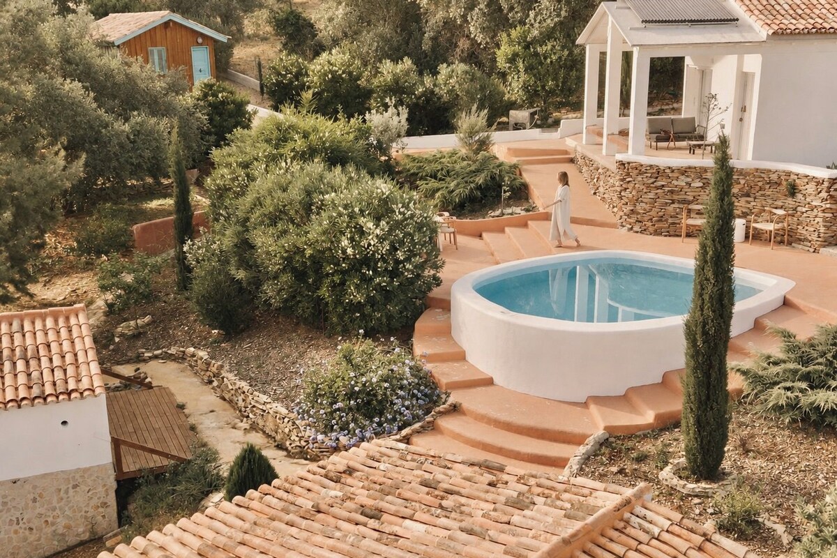 Zona de piscina con escalones de acceso, rodeada de vegetación y muros de piedra.