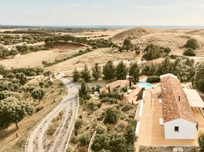 Un paisaje rural con un camino serpenteante, un edificio blanco con tejado de baldosas y una piscina.