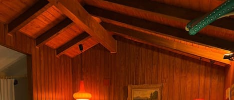 Un dormitorio con paneles de madera, una cama, una mesita de noche, una lámpara de pared y una pequeña mesa redonda.