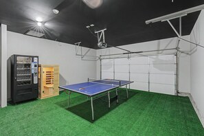 Ein Pingpongtisch mit Netz, ein Verkaufsautomat und eine Holzeinrichtung in einem Raum mit Kunstgrasebelag.