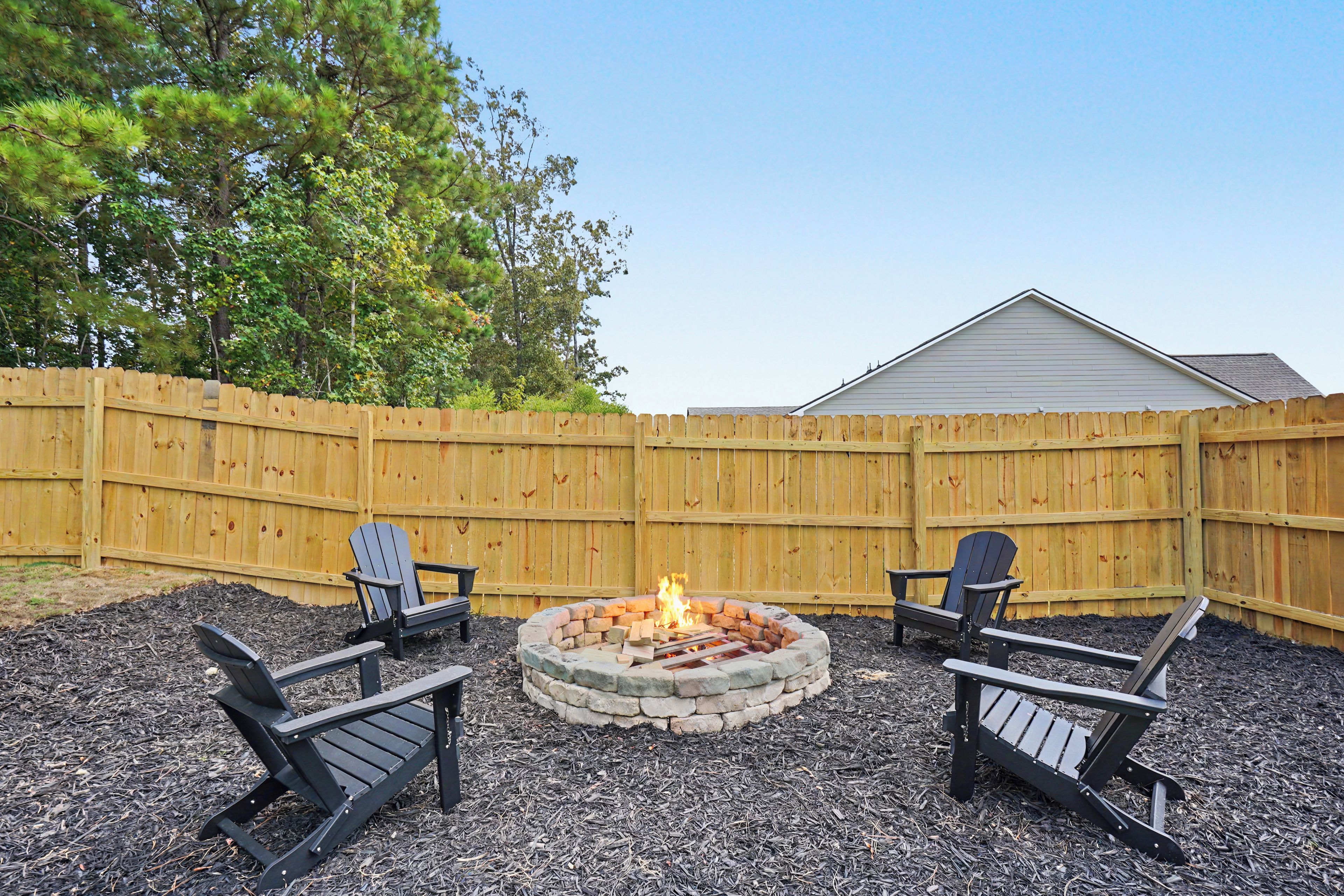 Un jardin avec un foyer, deux fauteuils Adirondack et une clôture en bois.