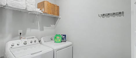 Un espacio para lavandería con lavadora y secadora, un estante con ropa doblada y un armario en la pared.