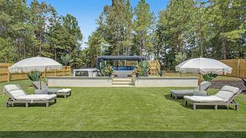 En trädgård med ett område för grillning, solstolar och en träaltan.