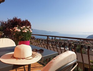 A balcony with a table, a chair, a potted plant with pink flowers, and a view of a town and mountains. - Tignale-olzano, Apt. 1 (Tignale)