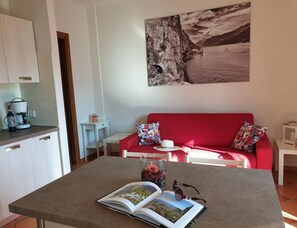 A modern living room with a red sofa, a coffee machine, and a large landscape painting on the wall. - Tignale-olzano, Apt. 1 (Tignale)