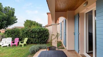A patio with a table and chairs, a covered area, and a building with blue shutters.