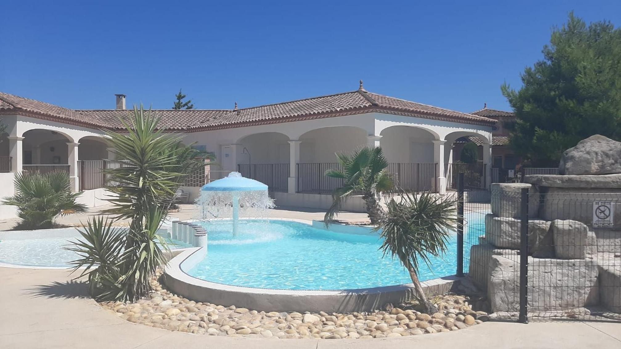 Una piscina con una fuente, rodeada de palmeras y un edificio con arcos.