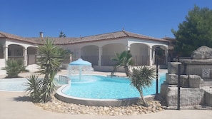 Una piscina con una fuente, rodeada de palmeras y un edificio con arcos.