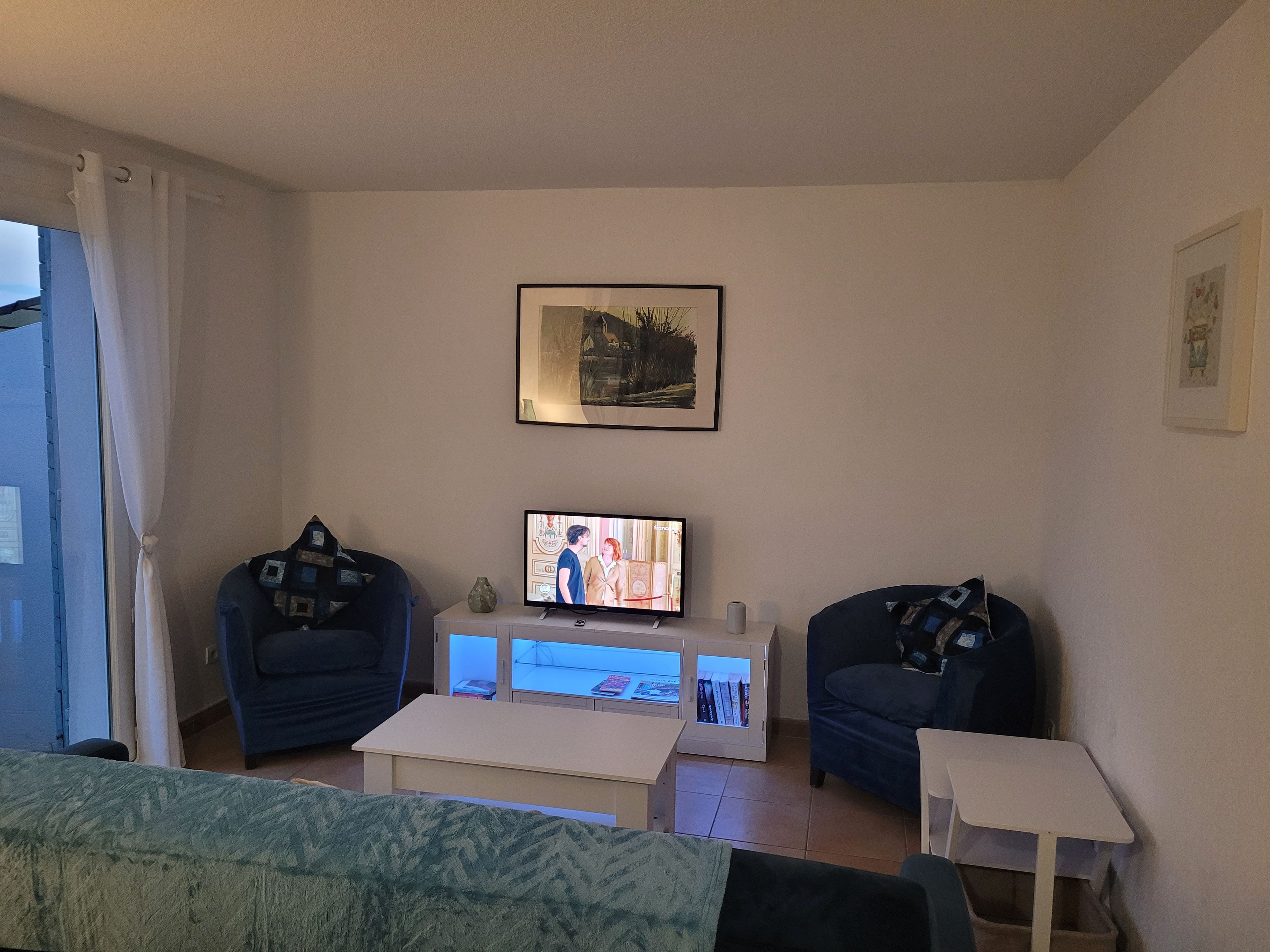 Una sala de estar con televisor, dos sillones, una mesa de centro y una estantería.