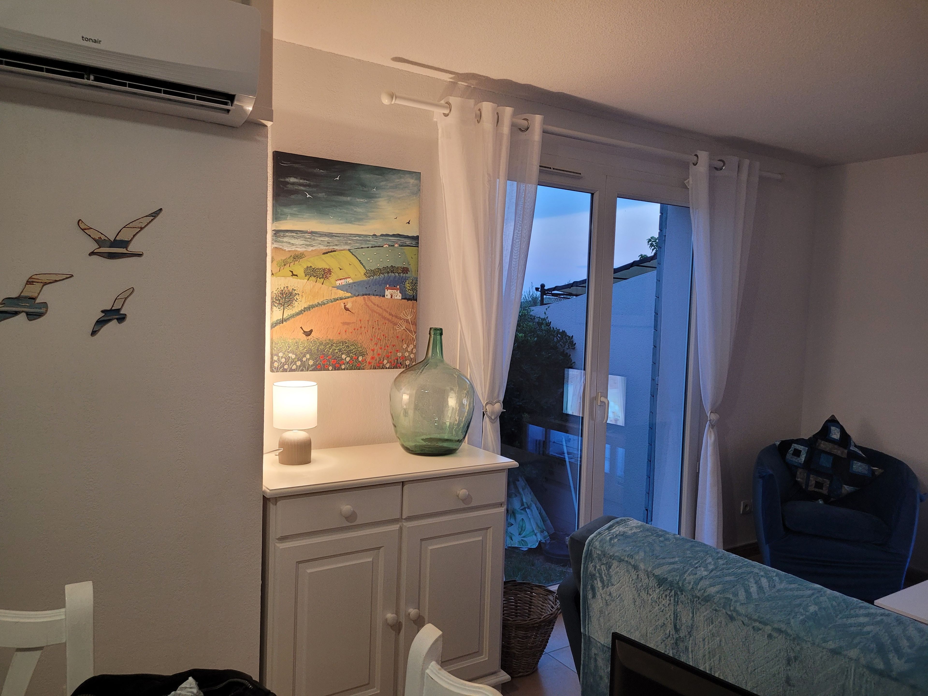Ett rum med en säng, ett skrivbord, en lampa, en tavla och ett fönster med gardiner.