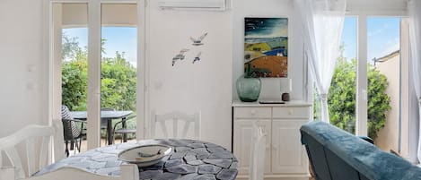 A dining area with a table and chairs, a painting, and a view of greenery outside.