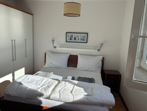Ein ordentlich bezogenes Bett mit weißer Bettwäsche, ein Kopfschild mit einem Bilderrahmen, ein Nachttisch und ein Kleiderschrank mit Schiebetüren.