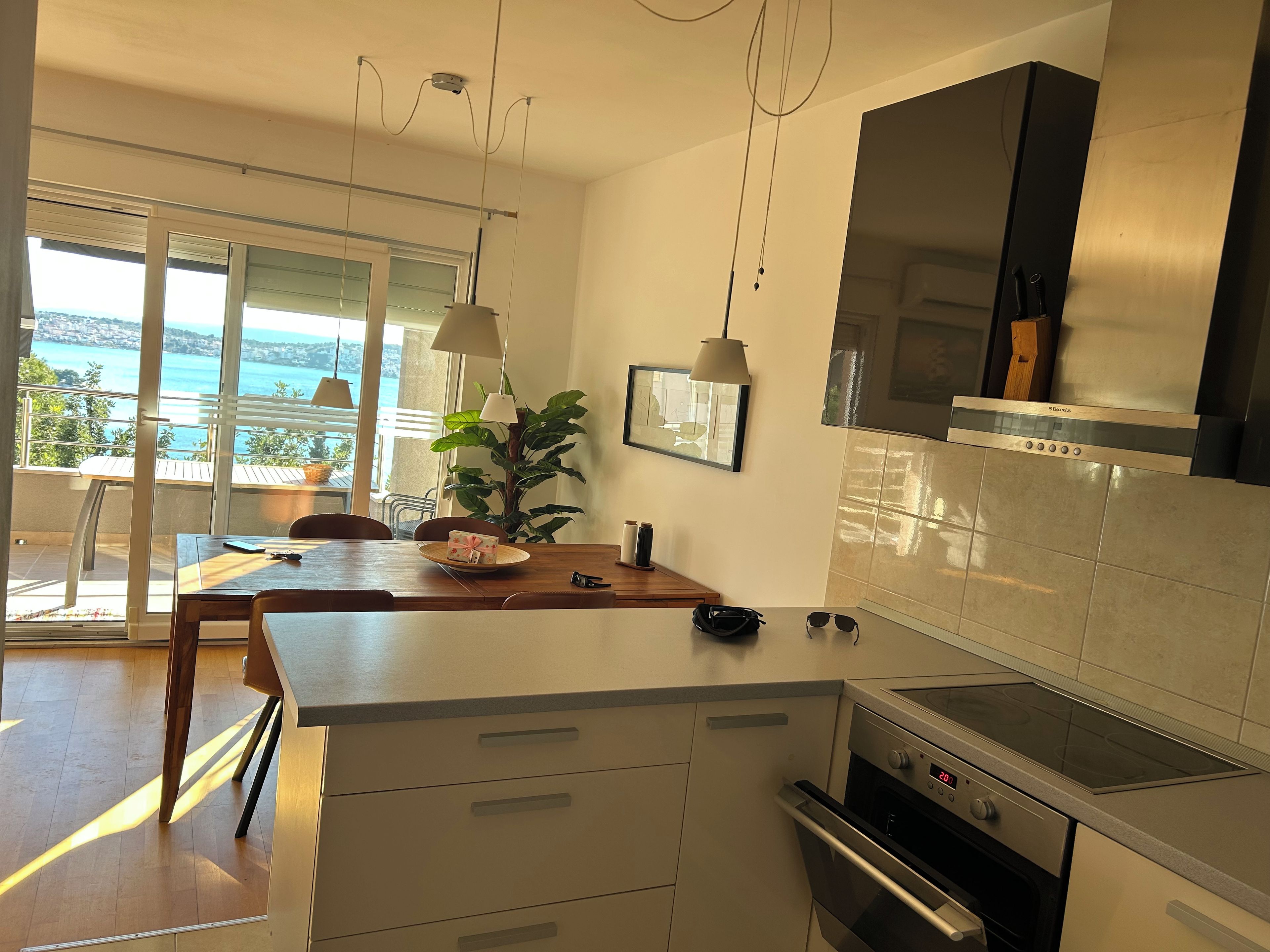 A modern kitchen with a view of the sea, a dining area with a table, and a large window.