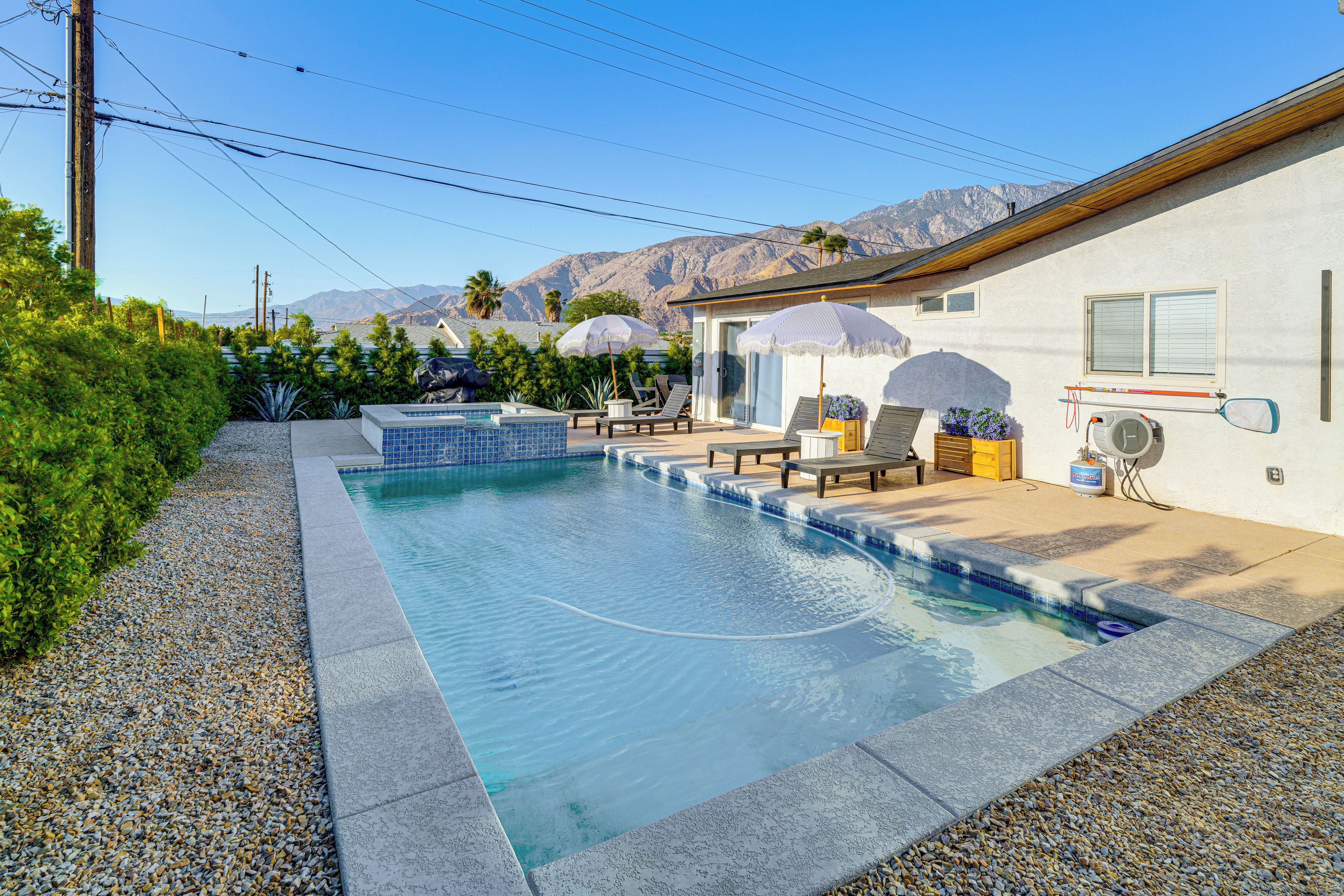 Piscina residencial con zona de patio, rodeada de jardín y con montañas al fondo.