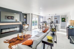A modern living room with a sofa, coffee table, and a dining area with chairs and a table. - Remodeled Home w/ Mtn Views in Palm Springs! (Palm Springs)