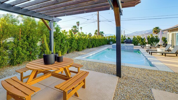 Ein Holztisch mit Bänken, ein Schwimmbecken und ein überdachter Bereich mit einer Pergola.