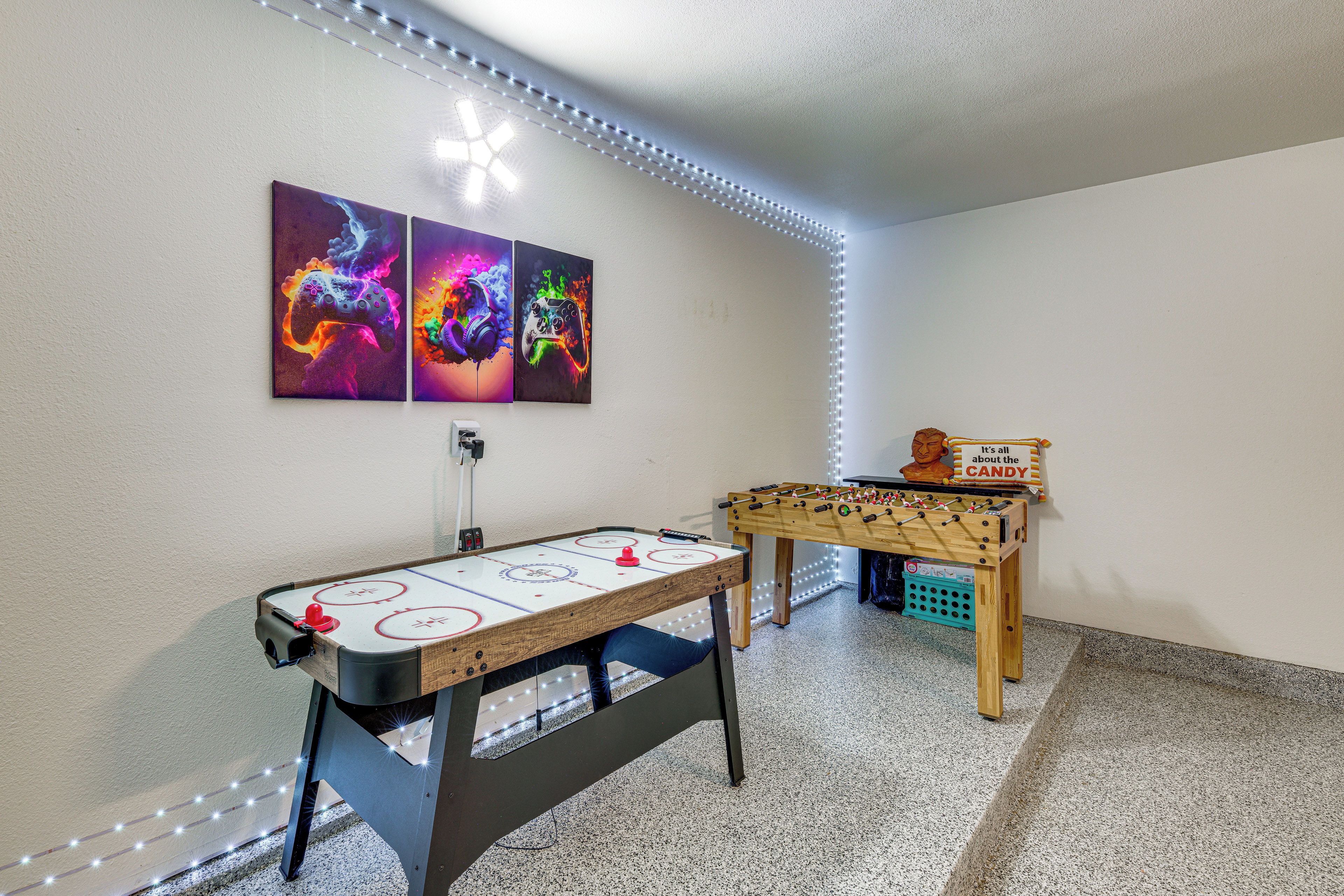 A room with an ice hockey table, a foosball table, and two wall-mounted gaming posters.