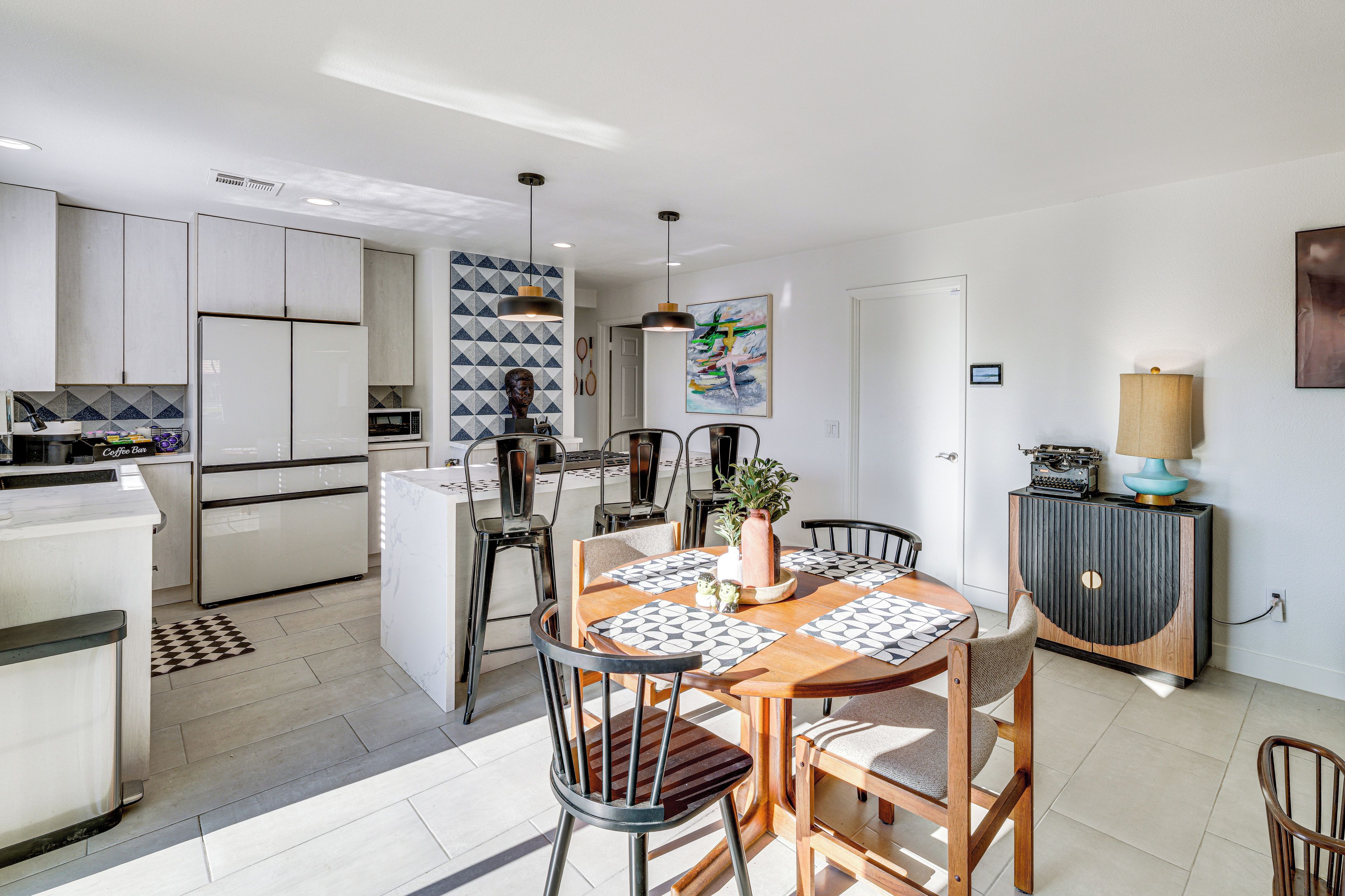 A modern kitchen with white cabinets, a dining area with a wooden table and chairs, and a kitchen island.