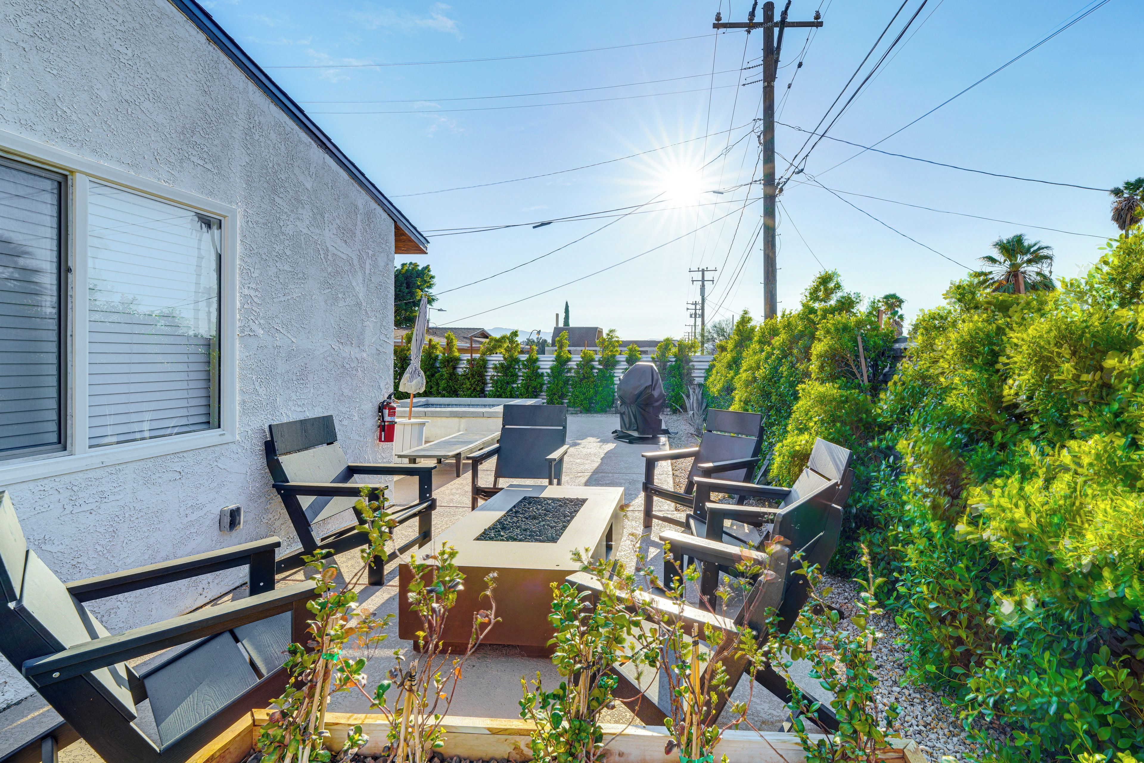 Un patio con mobiliario exterior, un extintor y vistas de la vegetación y edificios circundantes.