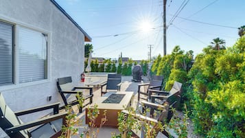 Un patio con mobiliario exterior, un extintor y vistas de la vegetación y edificios circundantes.