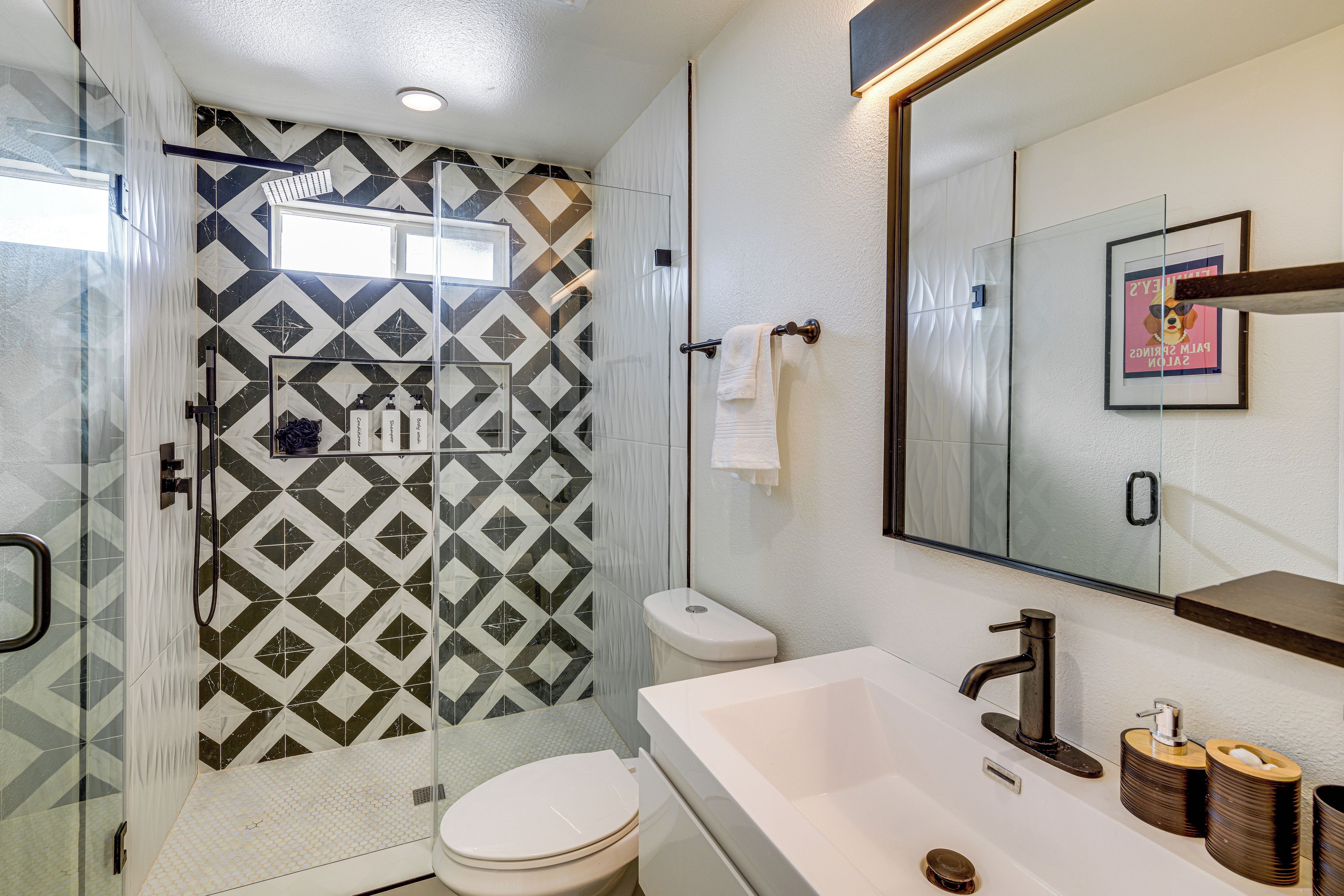 A bathroom with a shower, toilet, sink, and a mirror.
