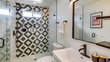 A bathroom with a shower, toilet, sink, and a mirror.