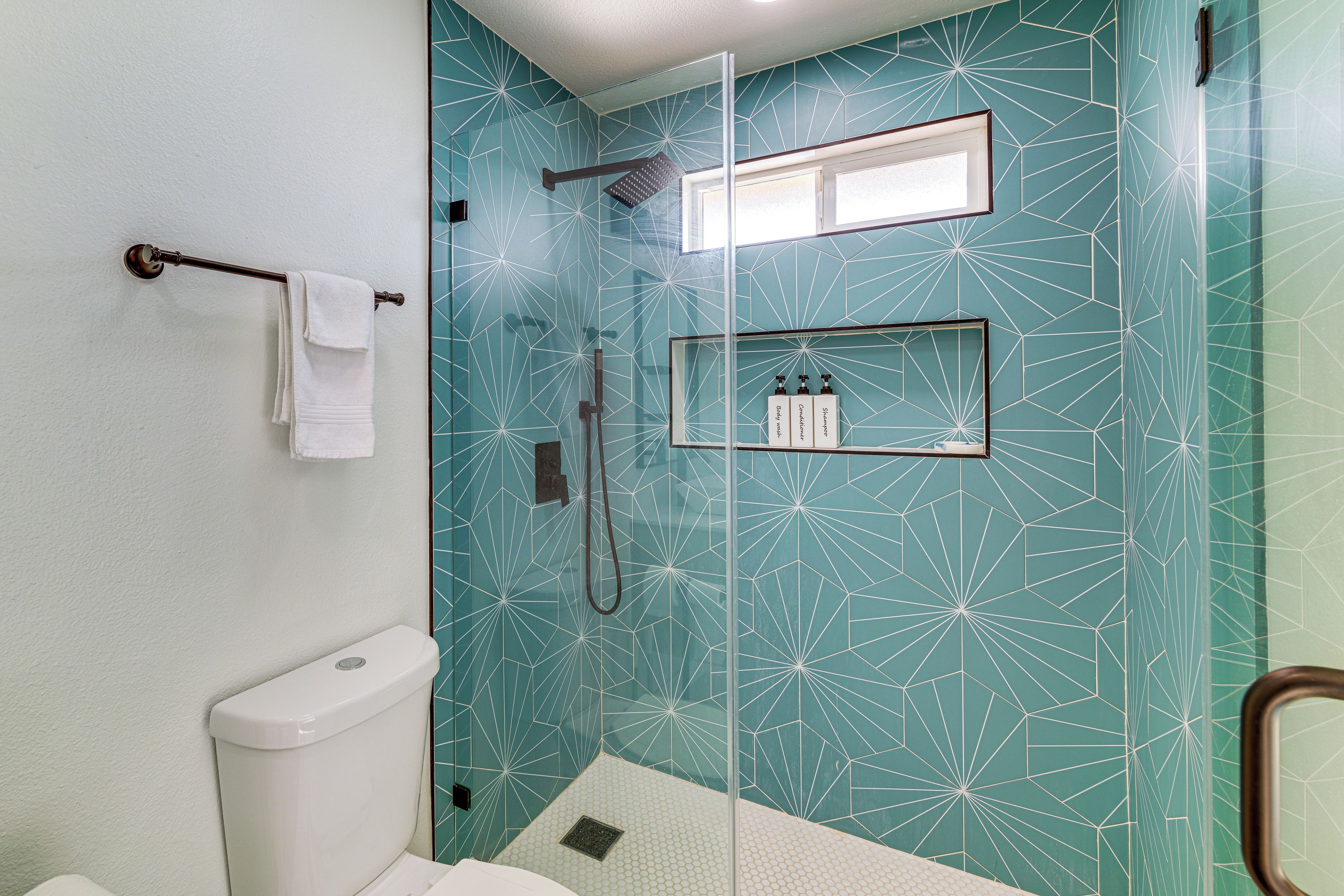 Une salle de bain avec une douche à parois de verre, des toilettes et une étagère contenant des articles de toilette.