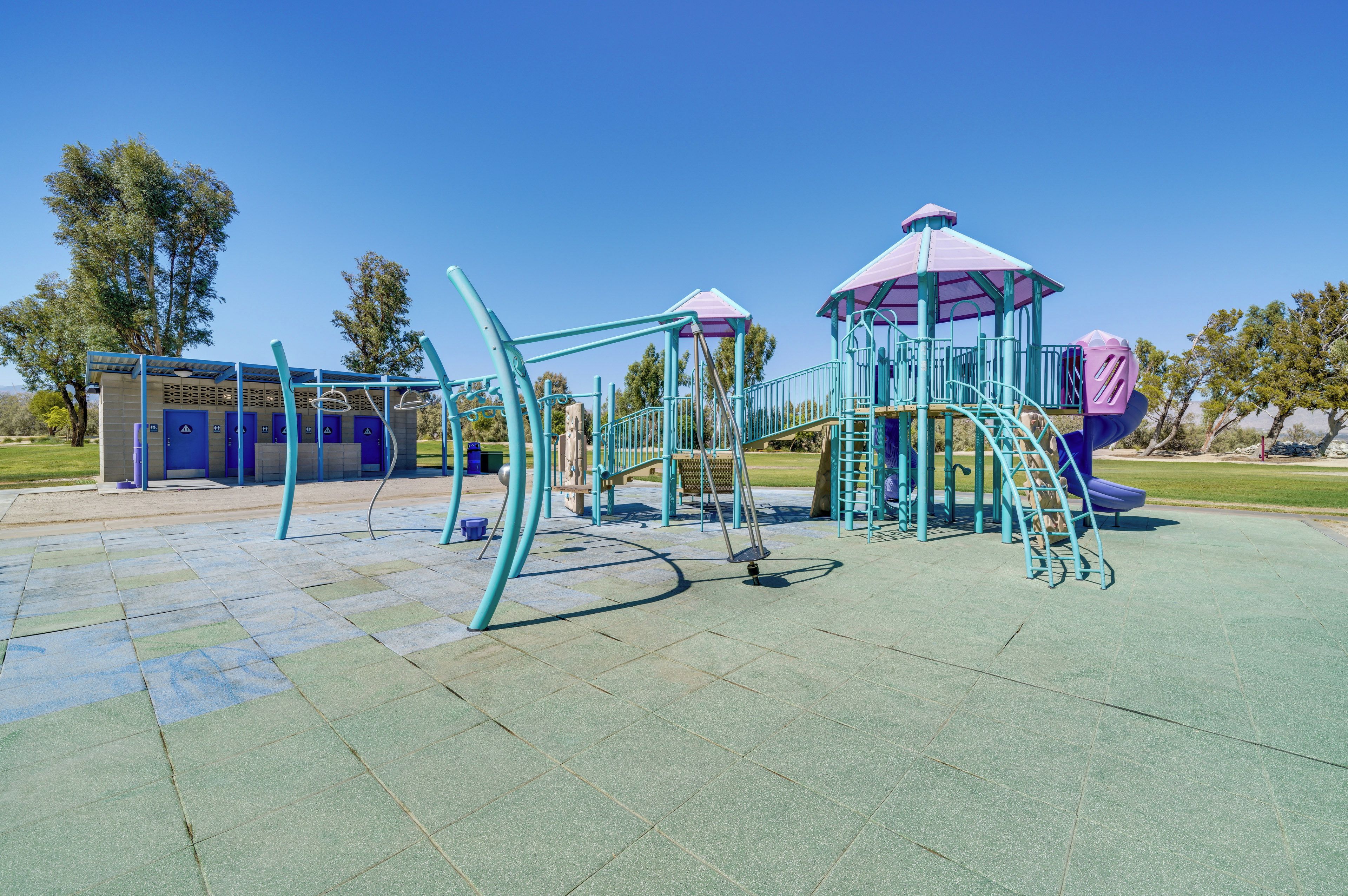 Un parque infantil con diversas estructuras de juego, incluyendo un tobogán y una estructura para escalar, bajo un cielo azul despejado.