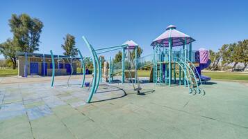 Un parque infantil con diversas estructuras de juego, incluyendo un tobogán y una estructura para escalar, bajo un cielo azul despejado.