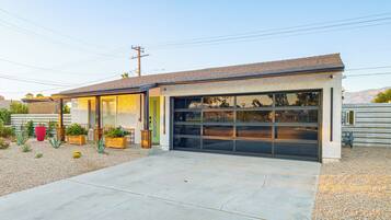 A single-story house with a garage, a small patio area with potted plants, and a clear sky.